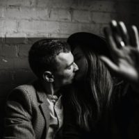 K&uuml;ssendes Paar auf einer Couch, die Frau hebt die Hand, da sie nicht fotografiert werden m&ouml;chte.