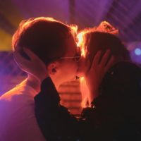 Zwei Menschen k&uuml;ssen sich auf einer sexpositiven Party im Hintergrund ist lila und blaues Licht zu sehen